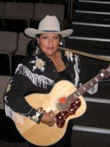 Arigon Starr playing her guitar in stage outfit
